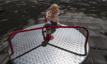Outdoor shot, little girl, 3 years old, blonde, playing on a merry-go-round, children's playground,