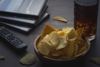 Bowl with crisps, remote control and drink on a dark table with DVD, stack