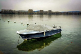 A solitary boat sits anchored in still waters, surrounded by gentle mist. The shoreline is faintly