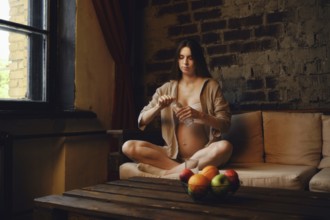 A pregnant woman sits comfortably on a sofa in her home, enjoying a moment of calm. She is focused