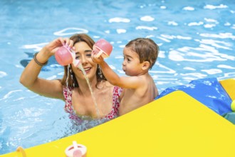 Mother and son enjoying playtime together, pouring water from pink toys in a bright yellow