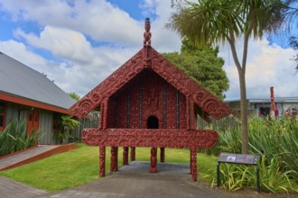 Small Maori building with red carvings surrounded by palm trees, New Zealand Maori Arts and Crafts