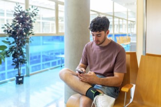 Patient sitting comfortably in a bright waiting room, using a smartphone to stay connected and