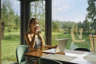 Woman working at bungalow in the woods on weekend and sipping mineral water from a glass