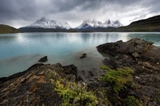 Cloudy mountain range Cuernos del Paine, shore of the blue lake Lago Pehoe in the evening light,