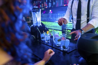 Bartender skillfully preparing vibrant blue cocktails garnished with fresh mint and ice in a lively