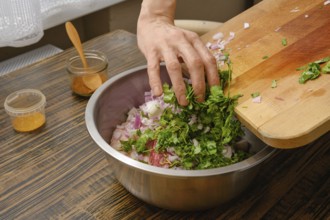 A hand adds freshly chopped cilantro and onions into a large metal bowl. The cozy kitchen