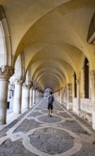 Young man walking through the portico of the Doge's Palace, St Mark's Square, Venice, Veneto, Italy