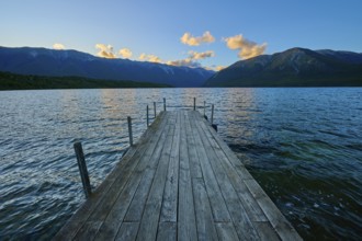 Wooden footbridge leading into a lake with mountains in the background at sunrise, summer, Lake