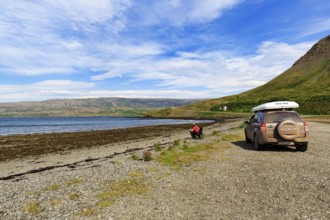 Tourist enjoying solitude in fjord landscape, SUV with roof tent, Skápadalur valley, coastline,
