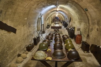 A tunnel with a row of helmets on a table, in the background exhibits, steel helmets, war museum,