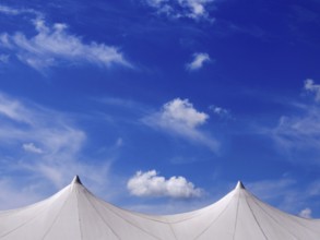 Exhibition tent under a bright blue sky adorned with fluffy clouds in a lively outdoor setting