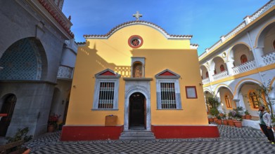 Yellow church with courtyard, cross and baroque elements, surrounded by plants, Holy Week, Bay of