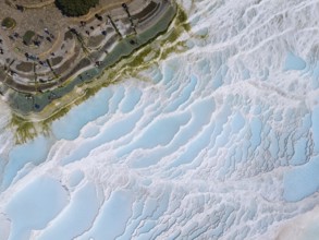 View of limestone terraces with blue water and small figures, surrounded by green vegetation,