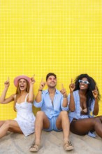 Group of cheerful multi ethnic friends pointing up while sitting on the sand against a vibrant