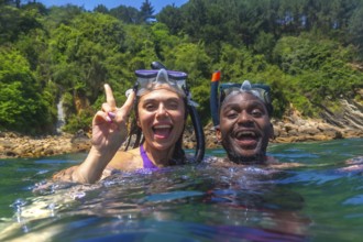 Young multi ethnic couple enjoying snorkeling together in crystal clear tropical sea, woman making