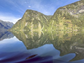 Mountains with reflections in the water against a blue sky in Doubtful Sound, South Island, New