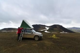 Barren volcanic landscape with snowfields, off-road vehicle with roof tent and ladder on mountain