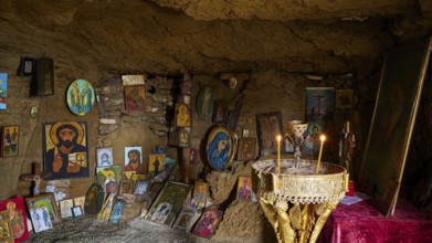 Icon-decorated cave altar with glowing candles, surrounded by religious artworks and paintings,