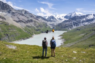 Two female friends throw their hats in the air, female mountaineers in front of a blue mountain