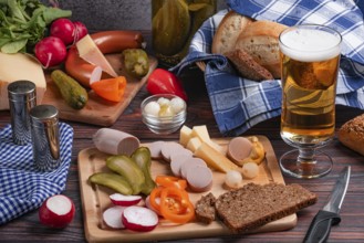 Rustic snack with sausage, cheese, beer, mustard, vegetables and bread on a laid table