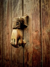 A vintage hand-shaped door knocker is mounted on a weathered wooden door, showcasing intricate