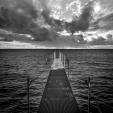 A serene jetty stretches over the calm waters of Lake Geneva, surrounded by dramatic skies filled