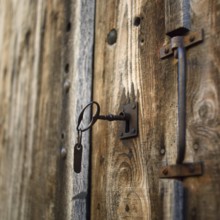 Close-up view of a rustic wooden door featuring a vintage lock and key. The texture of the wood and
