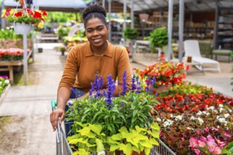 Smiling afro american woman pushing a shopping cart filled with vibrant flowers while browsing in a