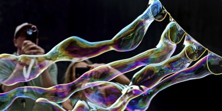 A man and a woman photograph iridescent soap bubbles in front of a black background,