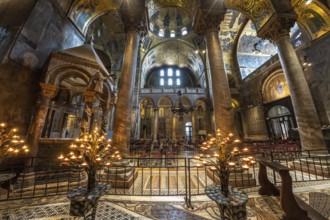 Lit candelabras illuminate the mosaic decorations and marble columns inside saint mark's basilica
