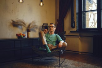 A middle-aged man sits in a chair and looks at the smartphone screen. He made an online order and