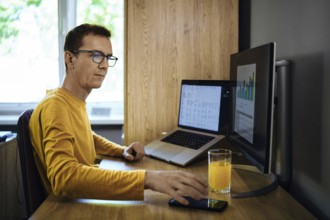 A man in a yellow shirt sits at a desk in a home office. He was distracted from studying statistics
