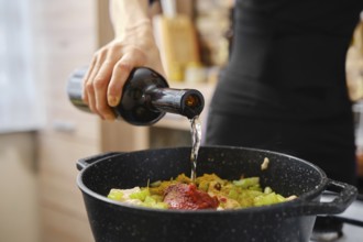 A hand pours liquid into a pot filled with chopped vegetables and sauce, creating a delicious