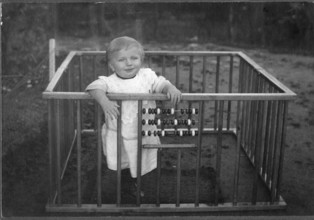 Child in a playpen, 1920s, A smiling child stands in a grid with an abacus in a nostalgic,