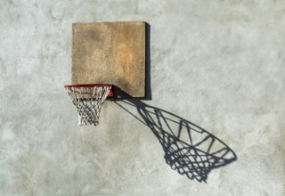 A worn basketball hoop is mounted on a textured wall, with the sunlight creating a captivating
