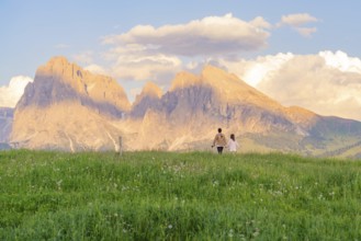 Couple in a meadow in front of picturesque mountains at sunset, Alpe di Siusi, Dolomites, South