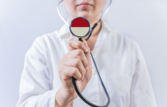 Female doctor holding stethoscope with Indonesia flag. National health system of Indonesia