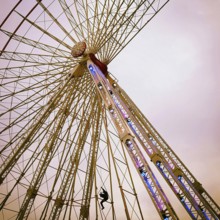 A maintenance worker is seen climbing the structure of a ferris wheel that features vibrant lights.