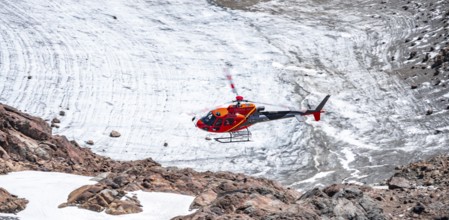 Red helicopter flies over glaciers in the mountains, Stubai Alps, South Tyrol, Italy