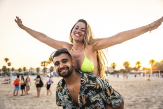 Carefree woman enjoying piggyback ride on man's back, spreading arms wide with joy on a sunny beach
