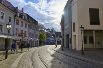 City street with railway tracks, lined with modern buildings and bustling with people, Freiburg im