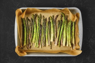 Roasted asparagus spears are neatly arranged on a baking tray lined with parchment paper