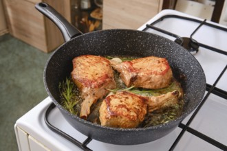 Three pork rib roasts are sizzling in a skillet, infused with fresh herbs while cooking on a