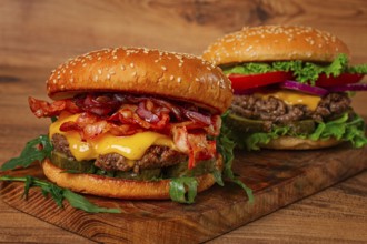 Two burgers with beef patty, fried bacon, cheddar cheese, tomatoes, homemade, no people