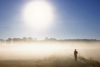 Man running on a dirt road in a rural landscape an autumn morning with low mist in backlight