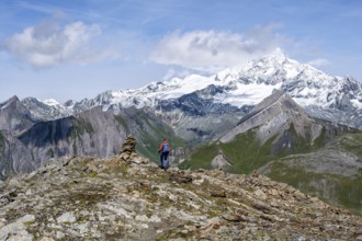 Female mountaineer on hiking trail with cairn, behind glaciated and snow-covered summit of the