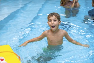 Young boy enjoying his summer vacation, playing and making funny faces in a swimming pool with a