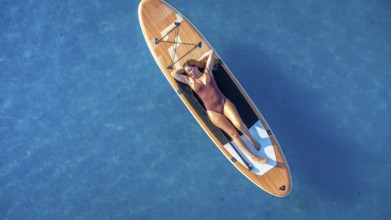 Lying on a paddle board, a woman enjoys the tranquility of the calm blue sea, soaking up the sun