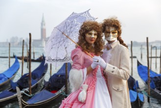Dressed up couple, posing with masks and parasol, Venetian costumes, gondolas at St Mark's Square,